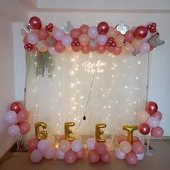 This bridal shower decoration features a balloon garland over a backdrop of sheer curtains and fairy lights. The "Bride to be" neon sign adds a modern glow, and I can spell out names or words with foil balloons, as seen here.
