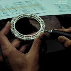 A close-up view of the polishing process. You can see the artisan's steady hand as they work on a diamond bangle, with the detailed design sheet visible in the background. This is precision work that requires immense focus.