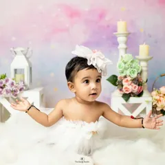 A dreamy portrait of a baby girl sitting in a cloud of fluff against a pastel-colored backdrop, creating a magical, ethereal look.