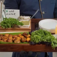 A member of our uniformed staff presenting a veg platter. This tray features roasted baby potatoes served on a banana leaf, accompanied by fresh parsley and green chutney, ready to be served to guests.