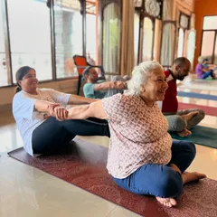 The spirit of our sangha, or community, is built on helping one another. Here, students of all ages, including a joyful senior practitioner, engage in partner yoga, sharing support and laughter. This shows that yoga truly is for everyone.
