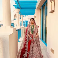 This bride looks absolutely regal against the stunning blue architecture in Doha. Her traditional red bridal lehenga is paired with makeup that highlights her features with a soft glow, perfect for a sunny destination wedding.