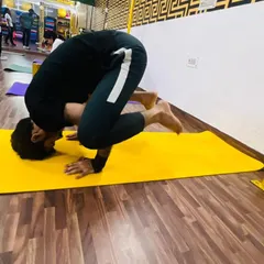A male student holding a strong crow pose. Our classes are for everyone, and we guide all our members to build strength and master challenging asanas.