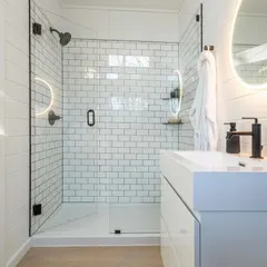 A close-up of a modern bathroom in one of our modular homes. The design features a clean, white-tiled shower, minimalist fixtures, and excellent lighting, proving that luxury is in the details.
