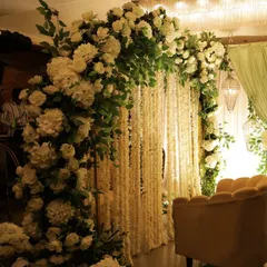An arch of lush white hydrangeas and roses set against a backdrop of hanging white floral strings (rajnigandha). This combination creates a beautifully fragrant and textured setting.
