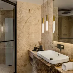 This bathroom is fully clad in richly veined beige marble for a seamless and opulent look. We used modern elements like a white vessel sink, a sleek black faucet, and a cluster of minimalist pendant lights to create a contemporary yet timeless design.