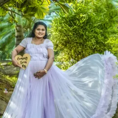 A beautiful outdoor solo portrait holding a "Coming Soon" sign. The flowing lavender gown and the lush green background create a soft and dreamy pregnancy announcement.