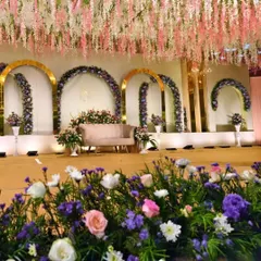A premium reception decor with a stunning ceiling of hanging pink and white flowers. The stage features golden arches adorned with purple and pink floral arrangements for a luxurious look.