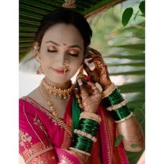 A beautiful bridal portrait of a Maharashtrian bride, capturing a quiet moment as she adjusts her earring. The details of her nath and green bangles are prominent.
