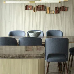 The dining area of the Jor Bagh Residence is highlighted by a dazzling brass installation and exquisite Makrana marble lights. Midnight blue upholstered chairs seamlessly offset the muted color palette of the wood-paneled walls.