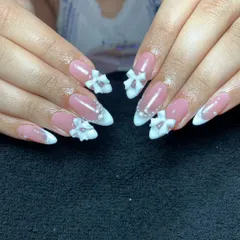 A classic French manicure gets an upgrade with 3D sculpted bows. This elegant design features white tips on almond-shaped nails, accented with delicate bows and pearls for a bridal or special occasion look.