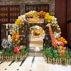 A spectacular jungle-themed entrance arch for a 'Lion King' birthday party. The arch is made of rock-patterned balloons and adorned with characters like Simba, Pumbaa, a giraffe, and a zebra, welcoming guests into the wild celebration.