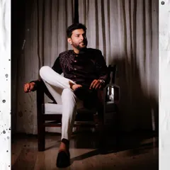 A dapper, full-length portrait of the groom seated, showcasing his modern-traditional Sangeet outfit.