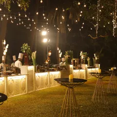 An evening view of one of my outdoor catering setups. The elegant white counters are backlit, and string lights create a magical ambiance for a wedding reception, perfectly complementing the delicious food.