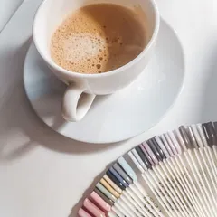 This is the lifestyle my courses can help you build. An aesthetic shot of coffee next to a wide array of nail color swatches, representing the creative world of a professional nail technician.