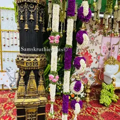 A detailed view of traditional decor elements, including a miniature temple pillar and hanging floral arrangements made of jasmine and purple flowers.