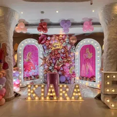 A glamorous Barbie themed birthday stage with light-up arched panels, a metallic balloon backdrop, and marquee letters.