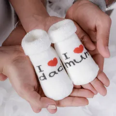 A close-up detail shot of parents holding a pair of tiny socks that say "I love mum" and "I love dad," a sweet announcement.