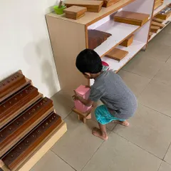 A child works with the Pink Tower, a classic sensorial material. This activity helps them visually discriminate between sizes and builds their understanding of dimensions, which is an indirect preparation for mathematics.