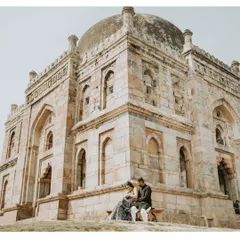 A quiet, romantic moment for a couple seated before a historic stone monument in Delhi, blending their modern love story with the echoes of the past.