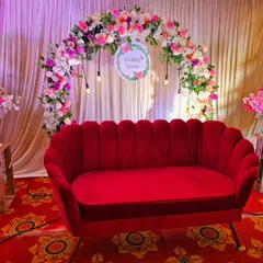 This classic setup is perfect for an engagement or anniversary celebration. A plush red sofa is placed before a beautiful arch of pink and white flowers against a simple curtain backdrop.