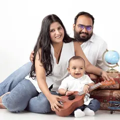 A travel-themed family portrait, with parents and their one-year-old son posing with vintage suitcases and a globe.