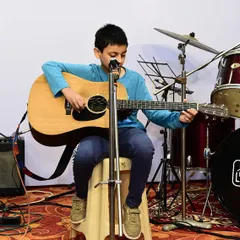 A young student confidently plays guitar and sings at our Student's Concert. We encourage students to become multi-talented performers, and our concerts are the perfect platform to showcase their hard work.