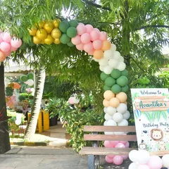 A beautiful balloon arch in jungle-themed colors, set up outdoors with a matching welcome sign.