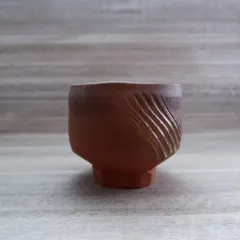 A Japanese-style earthenware teabowl, or 'chawan'. The carved wave-like pattern on the side provides a tactile experience, connecting the drinker to the object.