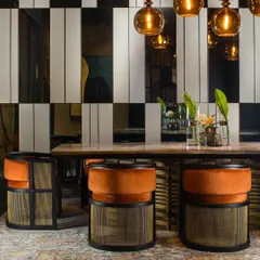 A closer look at our dining chairs, where plush orange velvet upholstery contrasts with a black matt frame and a brass-finished woven metal base. This piece is a study in combining different materials and textures.