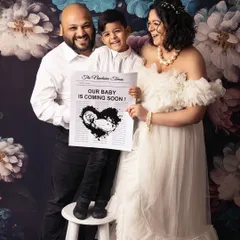 Announcing the big news with the whole family. The older brother proudly holds a sign while his parents look on with joy, all set against a romantic floral backdrop.