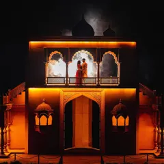A dramatic night shot that looks like a scene from an epic tale. The couple stands on a beautifully lit balcony, creating a powerful silhouette against a smoky, moonlit sky.
