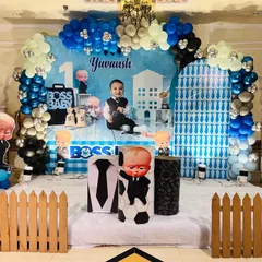 A wide shot of the Boss Baby themed birthday stage. You can see the full balloon arch, the personalized backdrop featuring the birthday boy, and all the character cutouts arranged on the stage.