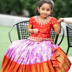 This little one looks so sweet in her custom Kanchi Pattu lehenga. The red embroidered blouse and the pleated lavender silk skirt with a wide orange and gold zari border is a classic and colorful combination.