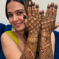 A happy bride showcasing her intricate grid-patterned mehendi that extends up her arms, perfect for her wedding day.