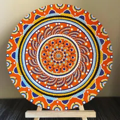 Here is a smaller dot mandala, displayed on an easel to show how it can be a beautiful tabletop decor item. The bright orange and blue design is full of energy and intricate detail.