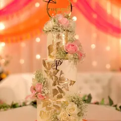 A beautiful three-tiered engagement cake with cascading fresh roses and baby's breath. The gold leaf accents and custom monogram add a touch of personalized luxury.