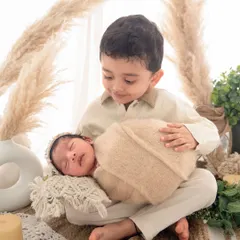 I love bringing creative themes to life, like this warm, boho-inspired setup. Here, a proud big brother holds his new sibling, showcasing how I can blend a stylized session with genuine family moments.