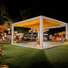 A modern, minimalist mandap for a Haldi ceremony, with a bright yellow draped ceiling and hanging wicker lamps, set against a vibrant tiled floor.