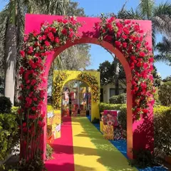 A bold and colorful entrance with a series of arches in bright pink and yellow, adorned with red and yellow flowers, creating a festive and welcoming vibe.
