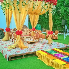 An outdoor mandap on a raised platform, featuring bright yellow drapes, red floral accents, and traditional seating for the wedding ceremony.