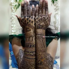 A shy bride or 'navri' peeking through her fully decorated hands. This shows a full-coverage design extending up to the elbows, ready for the wedding day.