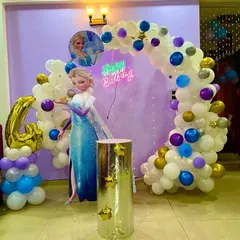 A magical Frozen-themed party for a 4th birthday, featuring an Elsa cutout, a balloon arch in shades of white, blue, and purple, and a neon "Happy Birthday" sign.