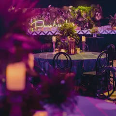 A view of the candlelit tables and neon signs being arranged for a glamorous cocktail night.