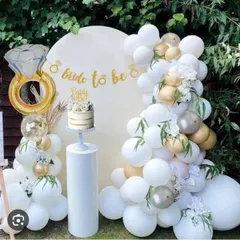 An elegant outdoor 'Bride to be' setup with a white and gold balloon arch, a custom backdrop, and a large diamond ring foil balloon.