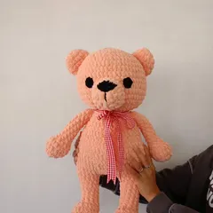 A close-up of the large pink teddy bear, showing its soft texture and the gingham ribbon tied around its neck.