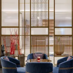 Intricately designed metal and glass screens separate the lounge from the lobby, offering privacy without enclosure. These bespoke elements feature patterns that add a layer of sophistication and visual interest to the space.