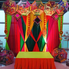 Pre-wedding functions should be full of color and joy. This vibrant backdrop for a Mehndi or Haldi ceremony uses colorful drapes and traditional Rajasthani embroidered umbrellas to create a festive and picture-perfect setting.