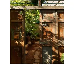 A weathered, rustic door opens to a garden path. The dappled sunlight highlights the texture and history of the upcycled wood, creating a seamless transition between the built and natural worlds.