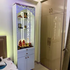 A close-up of the white pooja unit, showing the intricate jali-cut doors, backlit panel, and drawers for storing pooja essentials.